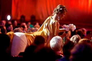 Ксения Собчак в образе кентавра раздает белые гвоздики гостям в зале.